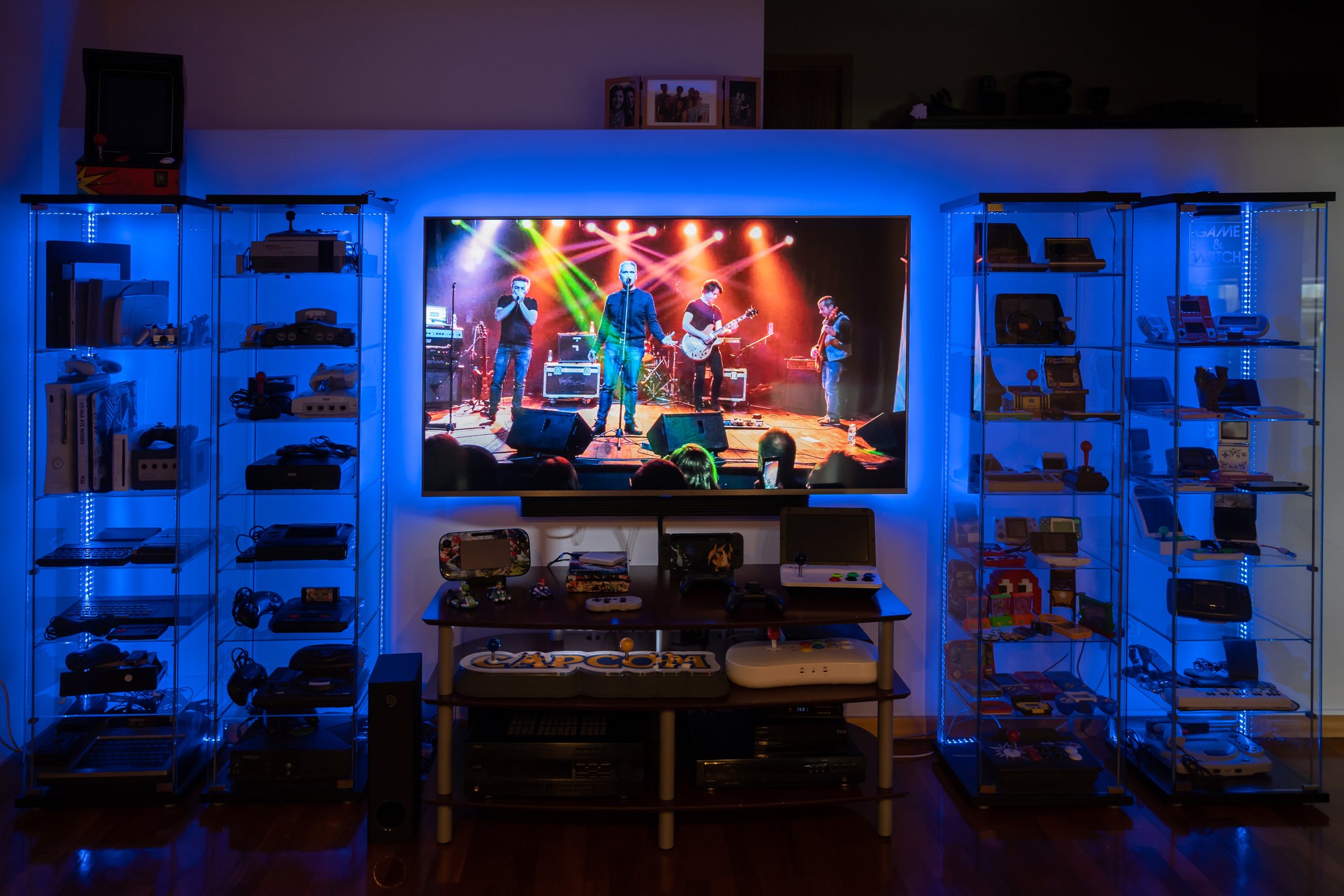 As quatro vitrines e a mesa com a coleção de consolas, iluminadas a azul, com a televisão ao centro